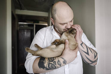 Tätowierter Mann kuschelt mit birmanischer Katze - EYAF00261