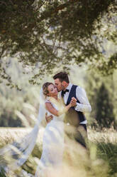 Romantic groom kissing bride on cheek in woodland - ISF21936