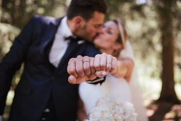 Romantic bride and groom kissing and showing wedding rings in woodland, selective focus on hands - ISF21943