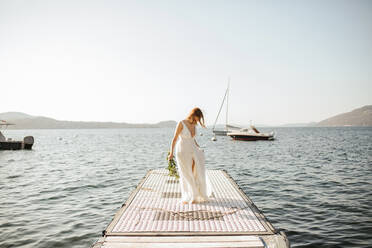 Junge Braut im Hochzeitskleid bei einem Spaziergang am windigen Seeufer, Stresa, Piemont, Italien - ISF21949