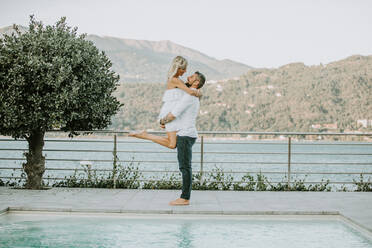Romantischer erwachsener Mann, der seine Freundin am Pool hochhebt, Porträt, Stresa, Piemonte, Italien - ISF21955