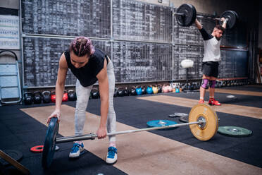 Junge Frau legt Hantelscheibe in die Stange im Fitnessstudio - ISF22015