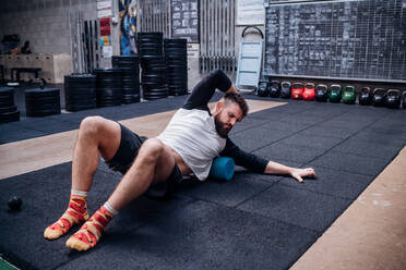 Young man massaging body with foam roller in gym - ISF22040