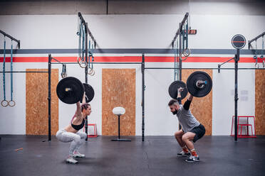 Junges Paar hockt und hebt Langhantel im Fitnessstudio - ISF22057