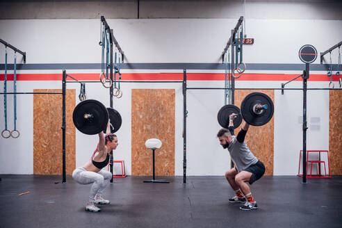 Young couple squatting and lifting barbell in gym - ISF22057