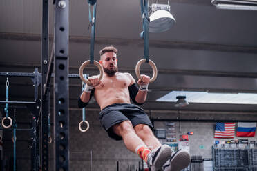 Junger Mann balanciert auf Gymnastikringen in der Turnhalle - ISF22070