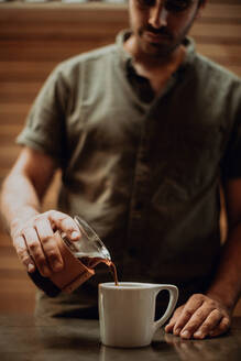 Barista gießt frischen schwarzen Kaffee in einen Becher auf dem Tresen eines Cafés, flacher Fokus - ISF22097