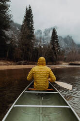 Young male canoeist rowing canoe on river, rear view, Yosemite Village, California, USA - ISF22105