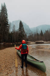 Junge Kanufahrerin bei der Vorbereitung eines Kanus im Fluss, Rückansicht, Yosemite Village, Kalifornien, USA - ISF22110