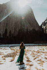 Junge Frau in langem Kleid in sonnenbeschienener verschneiter Berglandschaft, Rückansicht, Yosemite Village, Kalifornien, USA - ISF22117