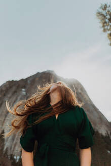 Junge Frau mit fliegendem Haar, die vor einem sonnenbeschienenen Berg aufblickt, Yosemite Village, Kalifornien, USA - ISF22119