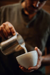 Barista gießt Milch in eine Kaffeetasse in einem Café, Ausschnitt mit geringer Schärfe - ISF22123