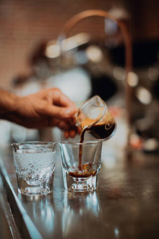 Barista gießt frischen Kaffee in ein Trinkglas auf dem Tresen eines Cafés, Detail der Hand, lizenzfreies Stockfoto