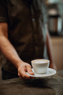 Barista, der eine Tasse Latte auf den Tresen eines Cafés stellt, Ausschnitt mit geringer Schärfe - ISF22131