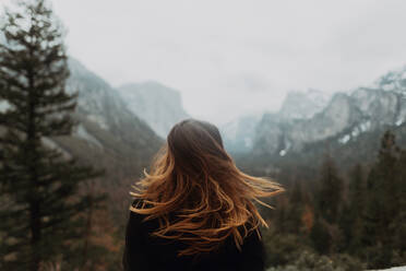 Young woman shaking long brown hair in mountain landscape, rear view, Yosemite Village, California, USA - ISF22133