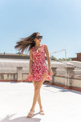 Porträt einer jungen Frau auf dem Dach in einem modischen Sommerkleid, die ihr Haar wirft - AFVF03428