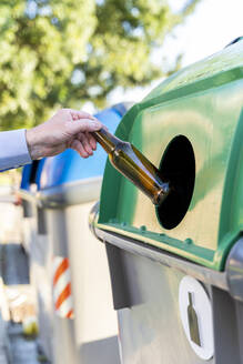 Nahaufnahme eines Mannes, der eine Flasche in einen Glascontainer stellt - AFVF03457