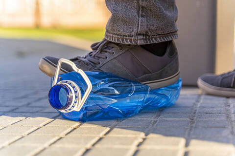 Close-up of man's feet sqashing plastic bottle for recycling stock photo