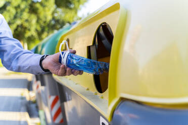 Nahaufnahme eines Mannes, der eine Plastikflasche in die Recycling-Tonne wirft - AFVF03462