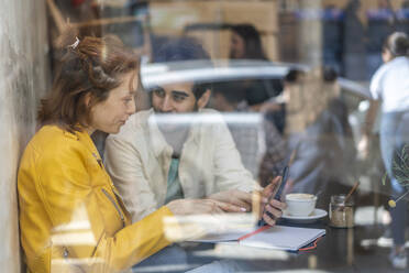 Mann und Frau mit Handy und Notizbuch treffen sich in einem Café - AFVF03479
