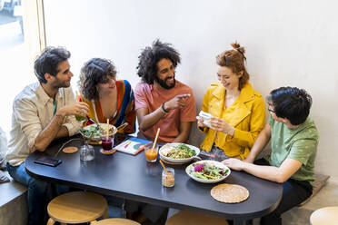 Gruppe von glücklichen Freunden mit einer Sofortbildkamera beim Mittagessen in einem Restaurant - AFVF03493