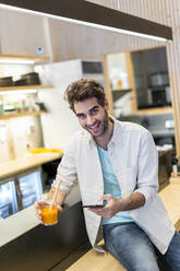 Portrait of a laughing man with cell phone sitting at the counter of a bar having a drink - AFVF03494