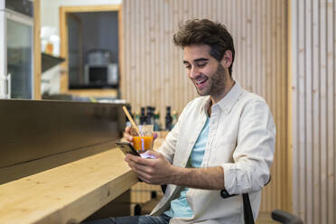 Mann mit Handy sitzt am Tresen einer Bar und trinkt etwas - AFVF03498