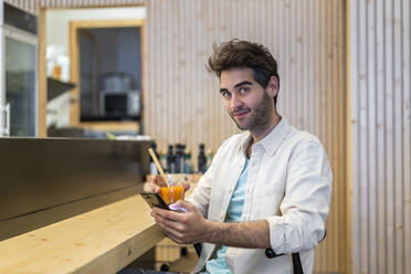 Porträt eines Mannes mit Handy, der am Tresen einer Bar sitzt und ein Getränk zu sich nimmt - AFVF03501