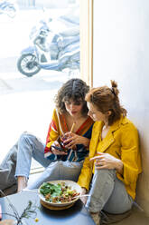 Zwei junge Frauen in einem Café schauen auf ihr Handy - AFVF03516