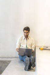 Man sitting on a step using laptop - AFVF03525
