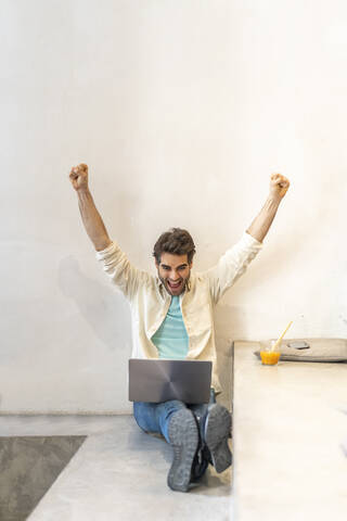 Jubelnder Mann, der auf einer Stufe sitzt und einen Laptop benutzt, lizenzfreies Stockfoto