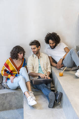 Drei Freunde sitzen mit Laptop und Getränk auf einer Treppe, lizenzfreies Stockfoto