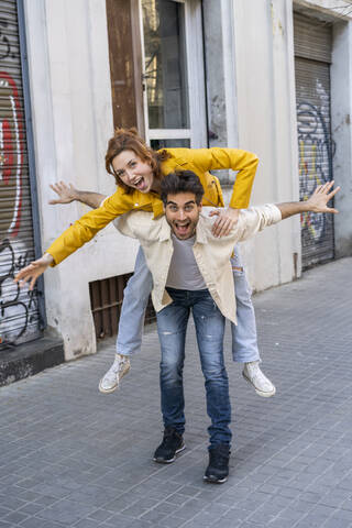 Happy man giving girlfriend a piggyback ride on pavement in the city stock photo