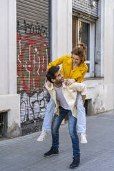 Man giving girlfriend a piggyback ride on pavement in the city - AFVF03536