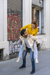 Mann nimmt seine Freundin auf dem Bürgersteig in der Stadt huckepack - AFVF03536