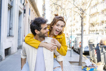Man giving girlfriend a piggyback ride on pavement in the city - AFVF03537