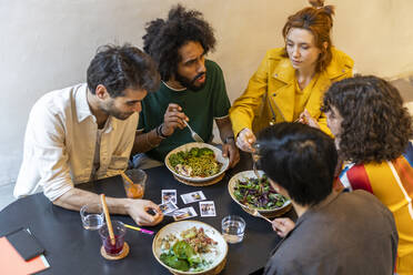 Eine Gruppe von Freunden isst in einem Restaurant zu Mittag und schaut sich Sofortfotos an - AFVF03554