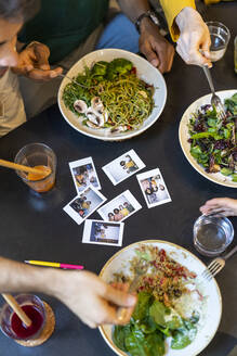 Gruppe von Freunden beim Mittagessen in einem Restaurant mit Sofortfotos auf dem Tisch - AFVF03555
