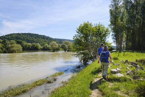 Rückansicht eines Mannes und einer Frau, die an einem sonnigen Tag an der Isar spazieren gehen, Bayern, Deutschland, lizenzfreies Stockfoto