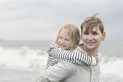 Porrait eines lächelnden Vaters, der seine Tochter huckepack am Meer trägt, lizenzfreies Stockfoto