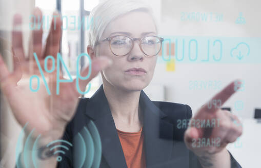 Businesswoman touching glass wall with data in office - UUF17905