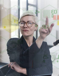 Geschäftsfrau berührt Glaswand mit Daten im Büro - UUF17908
