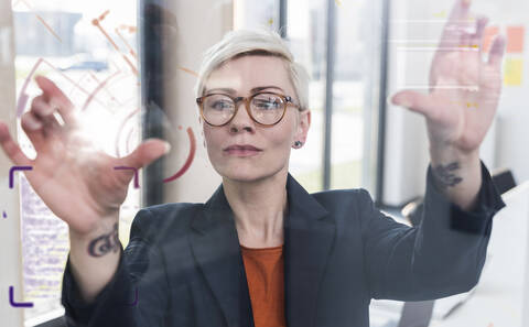 Businesswoman touching glass wall with data in office stock photo