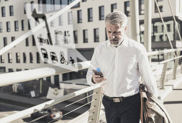 Mature businessman using cell phone for navigation in the city - UUF17914