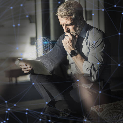 Mature businessman using tablet surrounded by virtual globe and lines stock photo