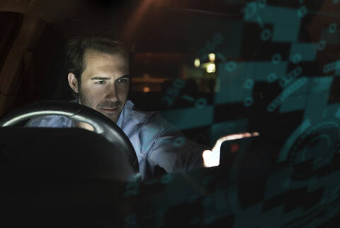 Geschäftsmann benutzt Gerät im Auto bei Nacht, umgeben von Daten, lizenzfreies Stockfoto