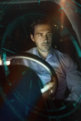 Geschäftsmann im Auto bei Nacht, umgeben von einem virtuellen Tachometer - UUF17926