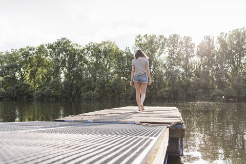 Junge Frau geht auf einem Steg an einem abgelegenen See spazieren, lizenzfreies Stockfoto