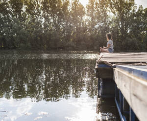 Relaxed woman sitting on jetty at a remote lake - UUF17931