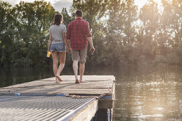 Young couple walking hand in hand on jetty at a remote lake - UUF17932